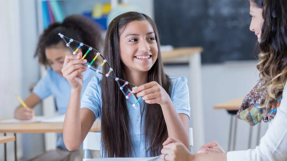 Una studentessa della Elite Preparatory Academy tiene in mano un modello di DNA sorridendo in classe.