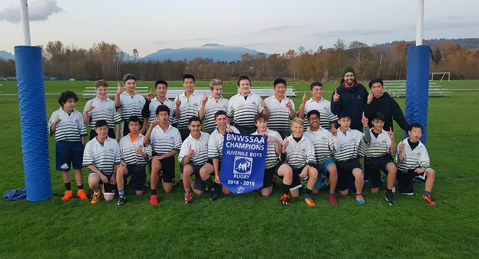 Un gruppo di studenti della Burnaby Mountain School si trova sul campo da calcio con le montagne sullo sfondo.