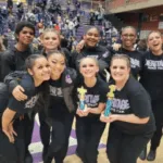 Grupo de estudiantes sonrientes vestidos de negro posan con trofeos en un pabellón deportivo