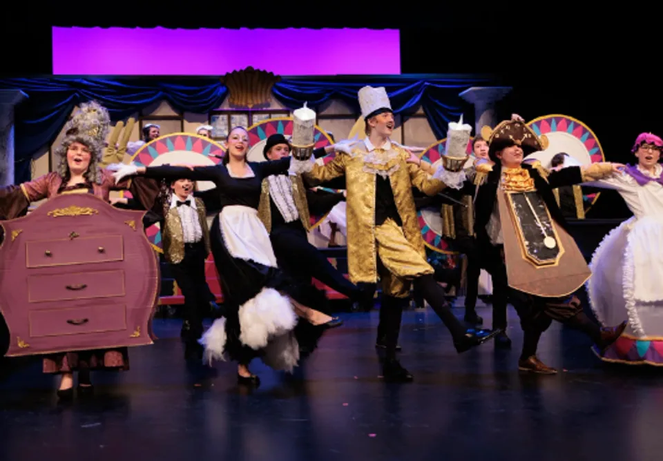 Un gruppo di studenti della Covenant Christian School sta su un palco con elaborati costumi davanti a uno sfondo teatrale colorato.