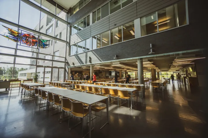 Atrio-mensa del campus con lunghi tavoli, ampie vetrate e aquiloni colorati appesi al soffitto