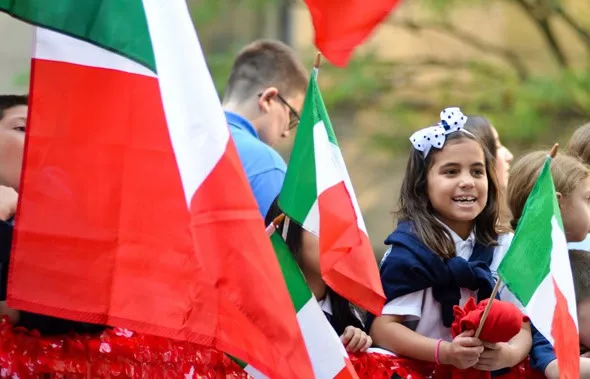 Niña sonriente con un lazo en el pelo sujetando una pequeña bandera de Italia
