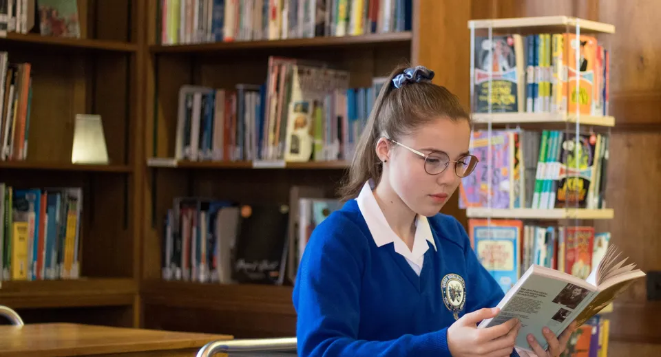 Una studentessa del Queen Ethelburga’s Collegiate legge concentrata un libro in biblioteca.