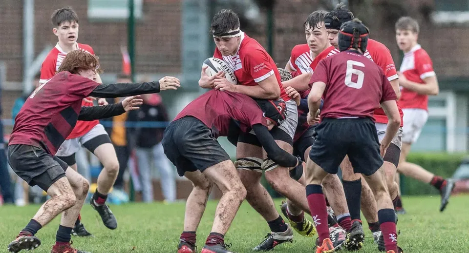 Studenti della Loughborough Grammar School giocano una partita di rugby su un campo da gioco con strutture sportive sullo sfondo.