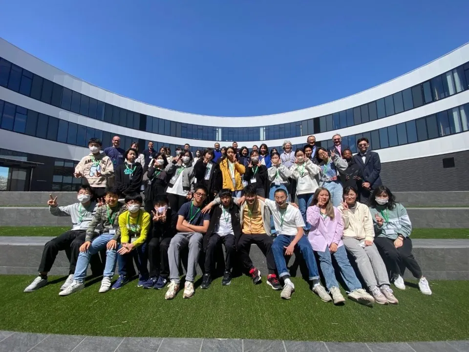 Eine Gruppe von Schülerinnen und Schülern posiert vor dem modernen, geschwungenen Gebäude des NUCB International College.