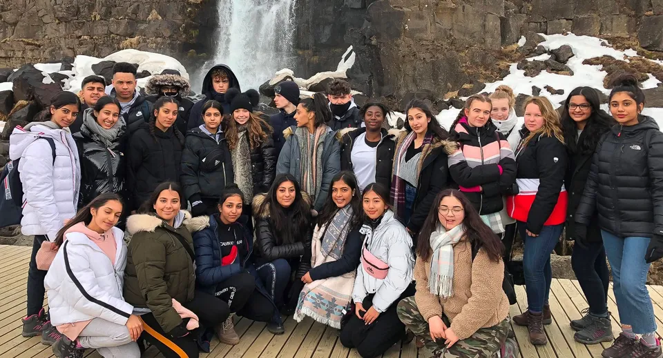 Un gruppo di studenti della The Royal School Wolverhampton in abiti invernali posa davanti a una cascata.