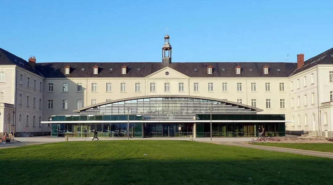 Historisches Schulgebäude mit gläsernem Eingangsbau hinter einer Rasenfläche