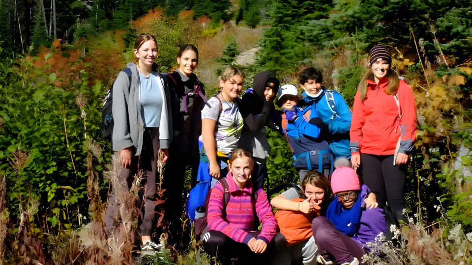 Studenti e studentesse della École des Sentiers-Alpins si trovano in un bosco con variopinte foglie autunnali.