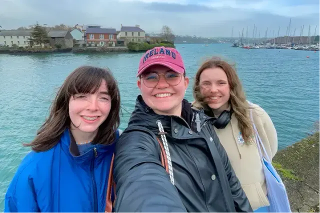 Tre studentesse si fanno un selfie sul porto di Cork, con barche a vela sullo sfondo