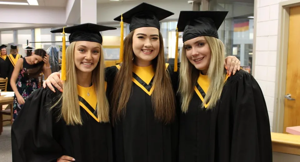 Tre studentesse con la toga da diploma posano per una foto nei terreni della Luther College High School.