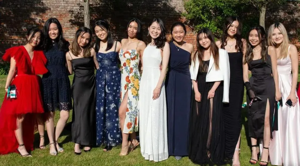 Un gruppo di giovani donne del Concord College posa davanti a un muro di mattoni circondato dal verde.