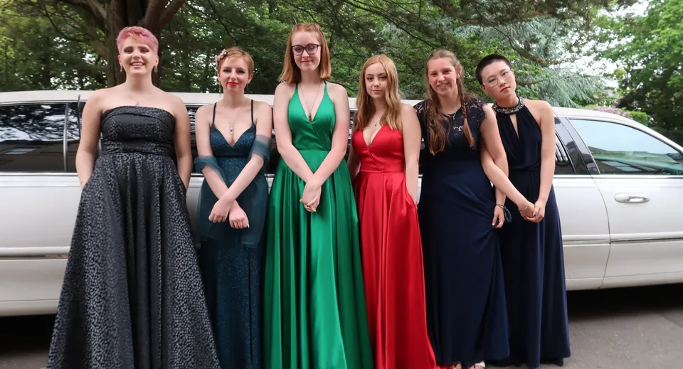 Un gruppo di giovani donne della Rathdown School posa davanti a una limousine bianca in un'area boschiva.