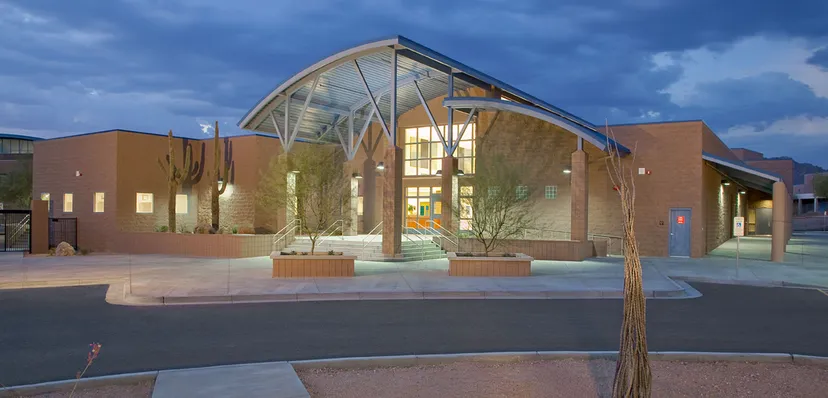 L'edificio moderno con facciata in vetro e tetto curvo nel campus del Cave Creek Unified School District è circondato da alberi.