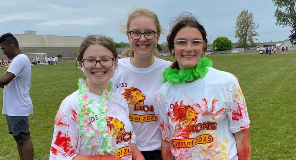 Tre studentesse della Leamington District Secondary School posano sorridenti all'aperto su un prato.
