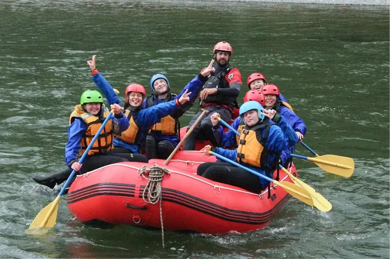 Gruppo di ragazzi con caschi e giubbotti di salvataggio fa rafting su un gommone rosso in un fiume
