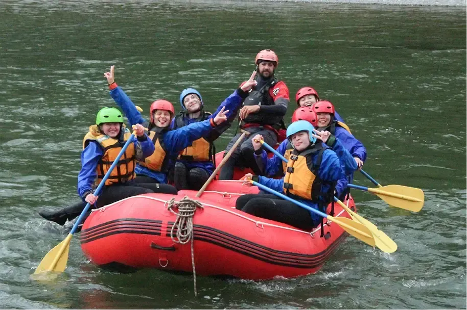 Gruppo di ragazzi con caschi e giubbotti di salvataggio fa rafting su un gommone rosso in un fiume