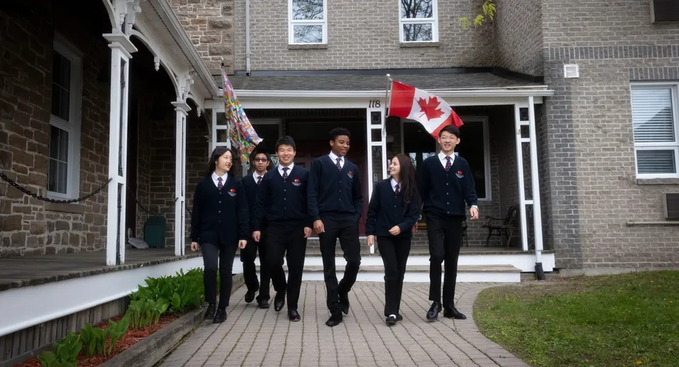 Studenti della Merrick Preparatory School in abito formale camminano insieme su un viale davanti a un edificio in mattoni con la bandiera canadese.