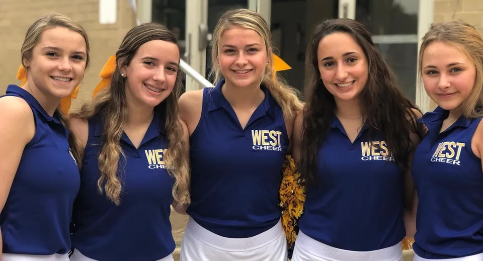 Cinque studentesse del Downingtown Area School District posano insieme con le loro divise da cheerleader in un impianto sportivo.