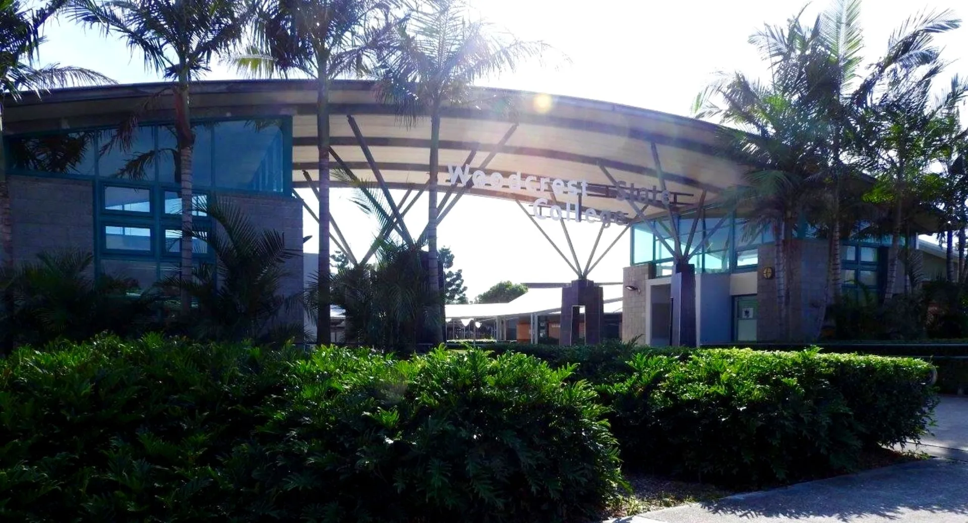 L'edificio moderno del Woodcrest State College si distingue per una struttura curvilinea in vetro e acciaio, circondata da un verde lussureggiante.
