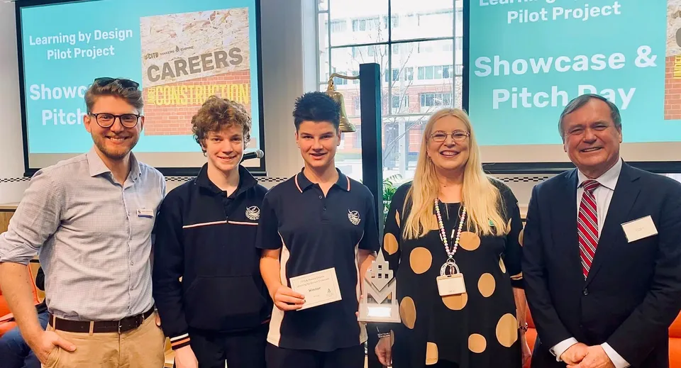 Un gruppo di studenti e un insegnante stanno davanti a un pannello informativo sul Learning by Design Pilot Project nel campus della Seaton High School.