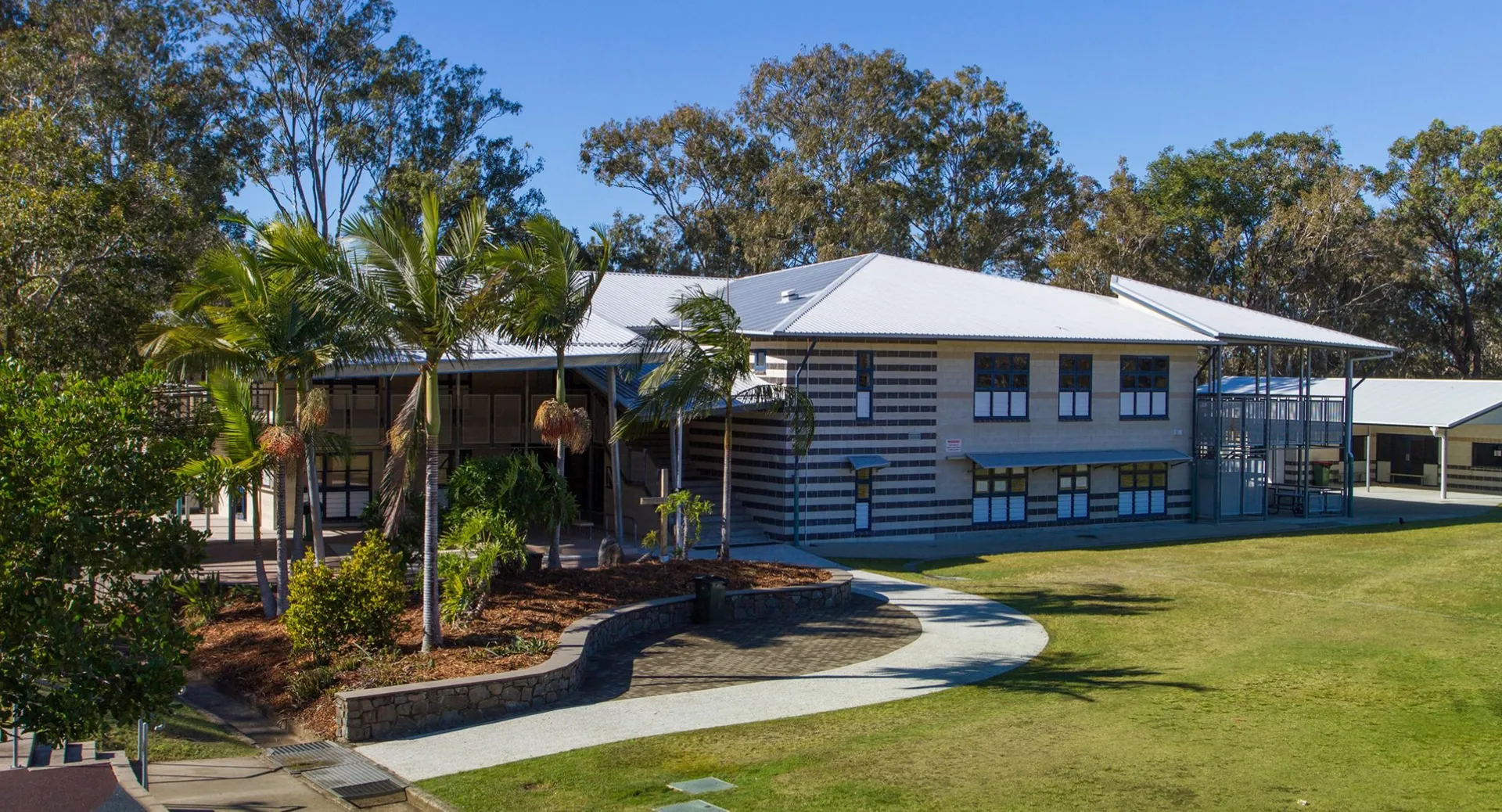 L'edificio in legno a due piani con tetto in metallo della Caloundra State High School è circondato da una rigogliosa vegetazione e palme.