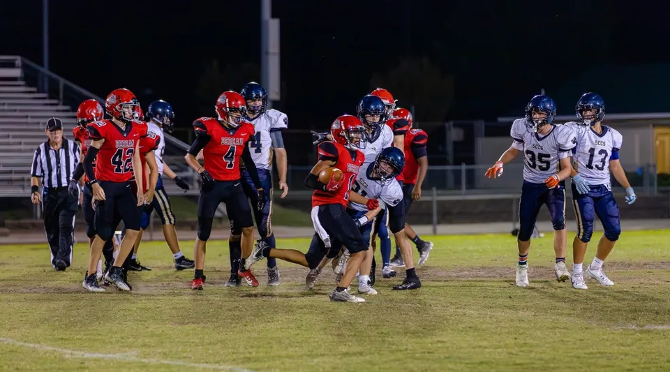 I giocatori della Berean Baptist Academy combattono sul campo sotto i riflettori durante una partita di calcio.