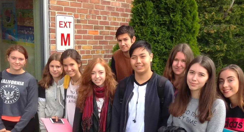 Un gruppo di studenti è in piedi davanti a un muro di mattoni con un cartello Exit nei terreni del Newcomb Central School District.