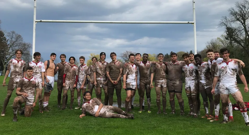 Un gruppo di studenti coperti di fango davanti a una porta da rugby sul campo sportivo del St. Andrew’s College.