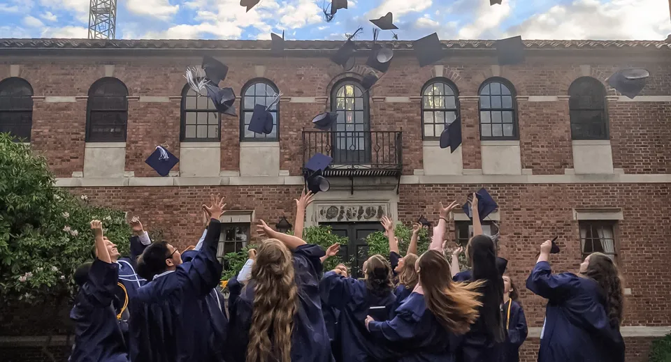 I diplomati e le diplomate della Covenant High School riuniti con toghe blu davanti a un edificio in mattoni con una torre.