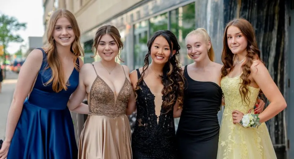 Cinque studentesse della Otago Girls High School posano sorridenti davanti a un edificio con finestre a vetri.