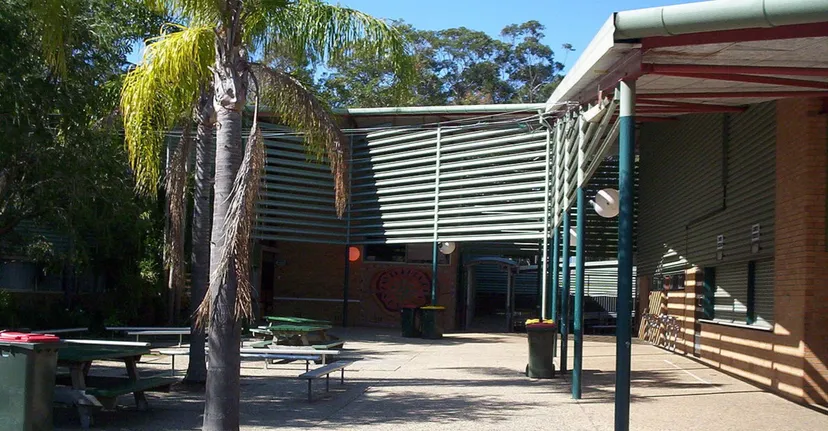 Il cortile della Woolgoolga High School mostra un'area con posti a sedere all'ombra con panchine in legno e molto verde.
