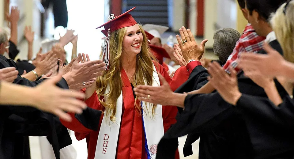 Una diplomanda in toga rossa viene festeggiata da una folla festante nel campus della Hackett High School.