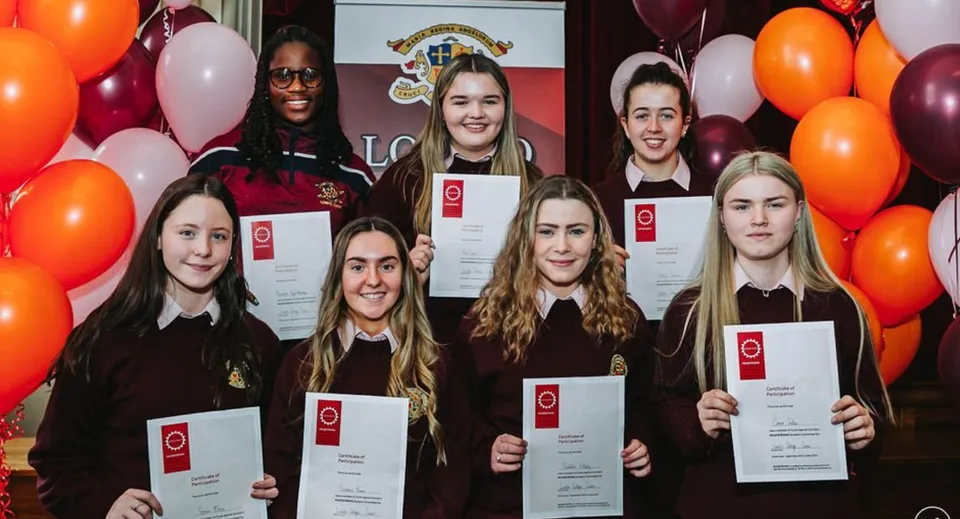 Un gruppo di giovani diplomate del Loreto College Cavan posa con i diplomi davanti a palloncini e al logo della scuola.