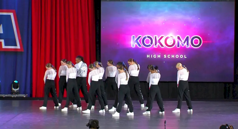 Studenti della Kokomo High School si esibiscono su un palco con il grande nome della scuola sullo sfondo.