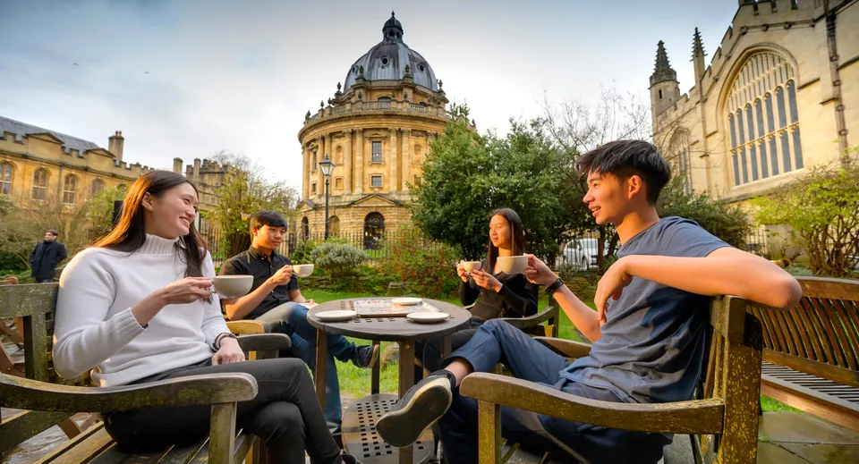 Un gruppo di studenti e studentesse chiacchiera e si gode delle bevande nell'area esterna dell'Oxford International College davanti a un edificio storico.