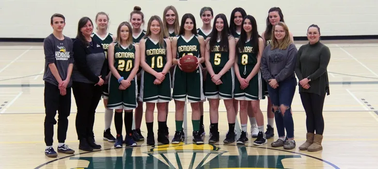 El equipo femenino de baloncesto de la Memorial Composite High School posa con camisetas verdes en el gimnasio.