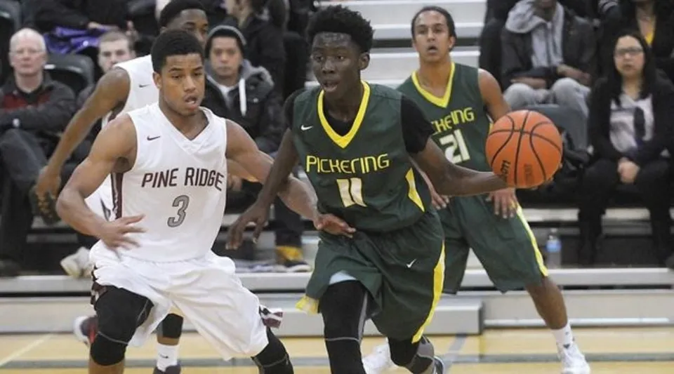 Due giocatori di basket lottano per la palla sul campo della Pine Ridge Secondary School davanti agli spettatori.
