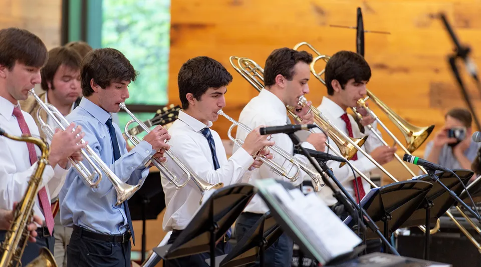 Un gruppo di giovani musicisti della Sidwell Friends School suona ottoni su un palco davanti a uno sfondo in legno.