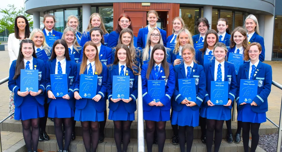 Un gruppo di studentesse in divisa blu si trova davanti a un edificio moderno della Assumption Grammar School.