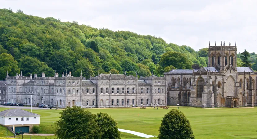 L'edificio principale storico della Milton Abbey School è circondato da alberi verdi e da un prato ben curato.