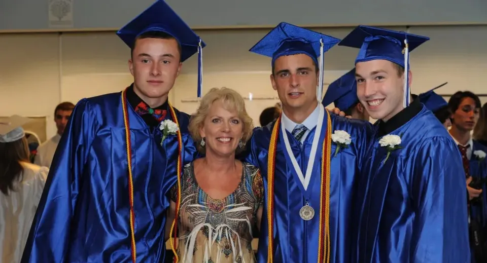 Tre studenti in toga blu e una donna con un abito colorato festeggiano insieme la cerimonia di diploma della Walpole High School.