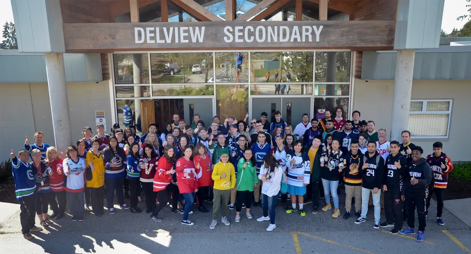 Un grande gruppo di studenti e membri dello staff si riunisce davanti all'edificio della Delview Secondary School.
