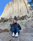 Estudiante sentada sobre unas rocas ante una gran formación rocosa de columnas