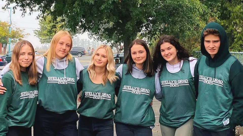Un gruppo di studenti e studentesse della Stellys Secondary School in maglia verde si trova all'esterno davanti ad alberi ed edifici.