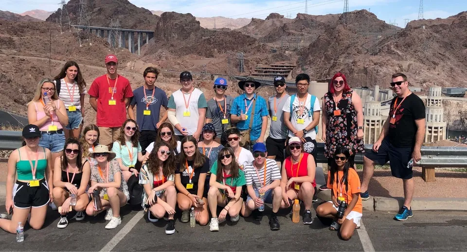 Un gruppo di studenti della Hillcrest High School posa davanti a uno scenografico paesaggio montano con un ponte sullo sfondo.