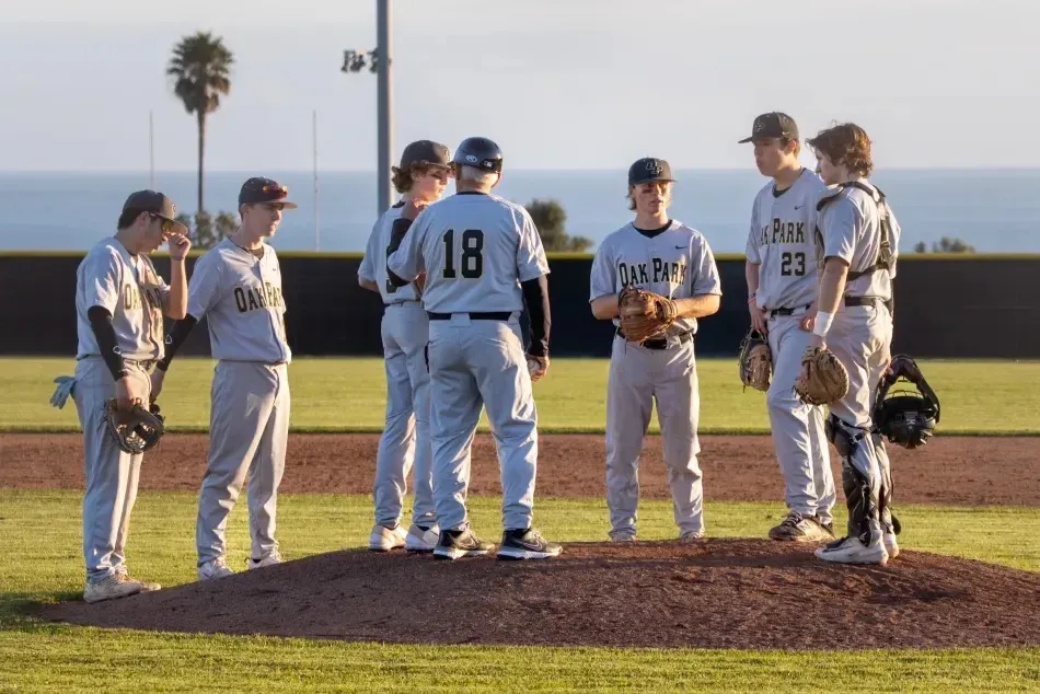 Un grupo de estudiantes de béisbol está de pie en el campo de béisbol de Oak Park Unified School District frente a palmeras y un cielo despejado.