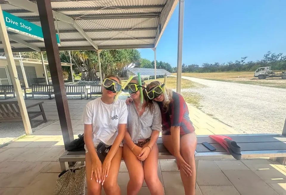 Drei Mädchen mit Schnorchelmasken sitzen auf einer Bank vor einem Tauchshop in Australien