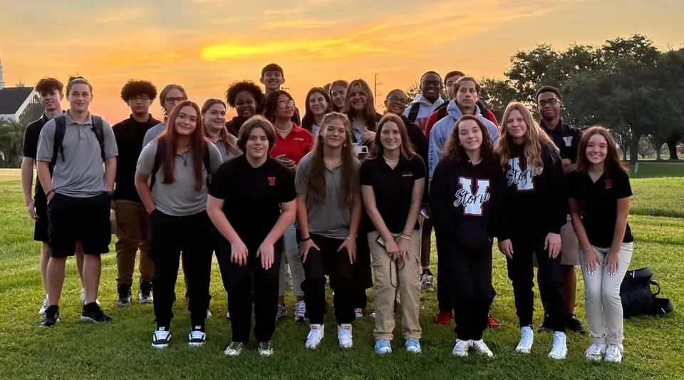 Un gruppo di studenti della Victory Christian Academy si trova all'aperto davanti a un tramonto con alberi sullo sfondo.