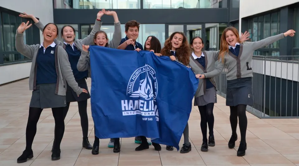 Un gruppo di studenti della Hamelin-Laie International School tiene insieme una grande bandiera blu con la scritta Hazelip.