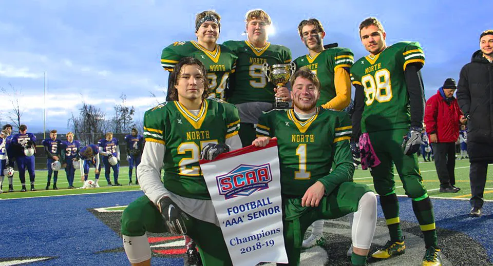 Giocatori di calcio del Barrie North Collegiate Institute tengono uno striscione del campionato sul campo da gioco davanti agli spettatori.
